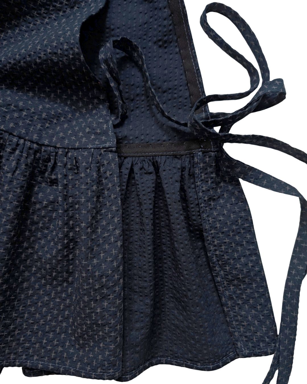 Close-up of a dark navy blue patterned  with a textured woven fabric, featuring a gathered waist and side ties.