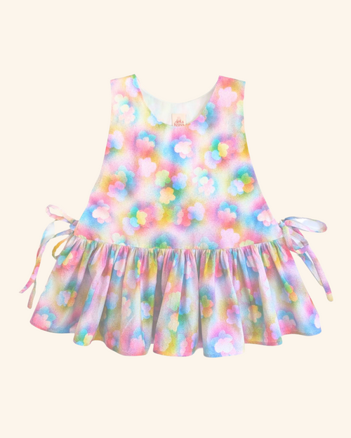 A sleeveless top with a pastel rainbow tie-dye watercolour pattern and a ruffled hem, featuring side tie details, shown against a solid cream background.