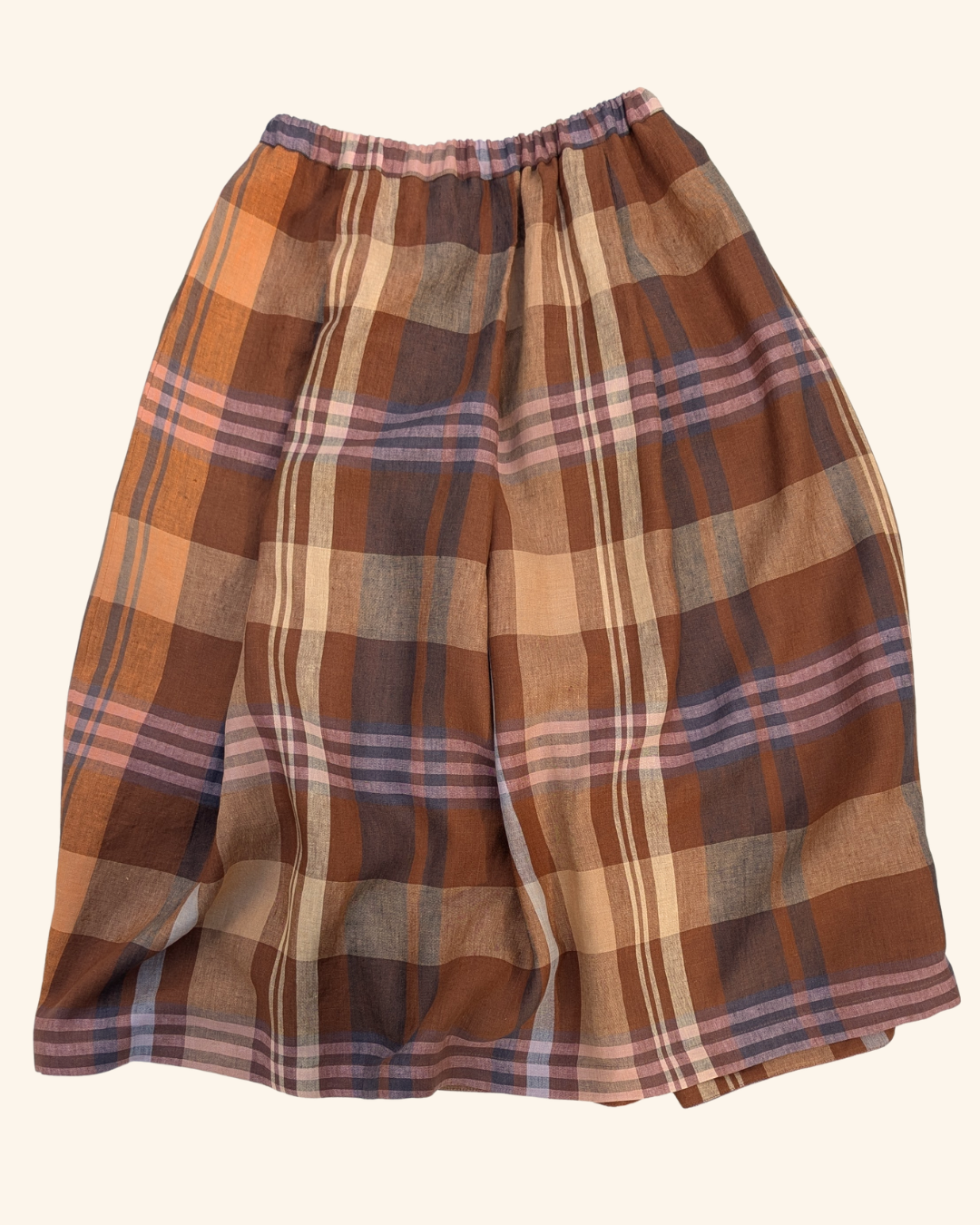 A plaid pleated skirt in earthy tones of brown, beige, orange, and muted purple, shown flat against a light cream background.
